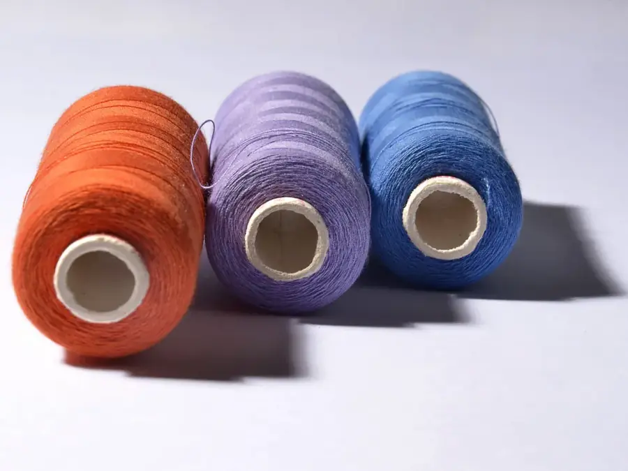 Three cones of yarn in orange, violet and blue standing on a pale surface